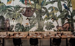 A hotel dining area with a row of decorated tables next to a wall with plant and animals on the tiles.