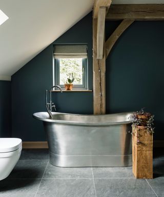 matt silver roll top bath in bathroom with sloped ceiling and blue wall