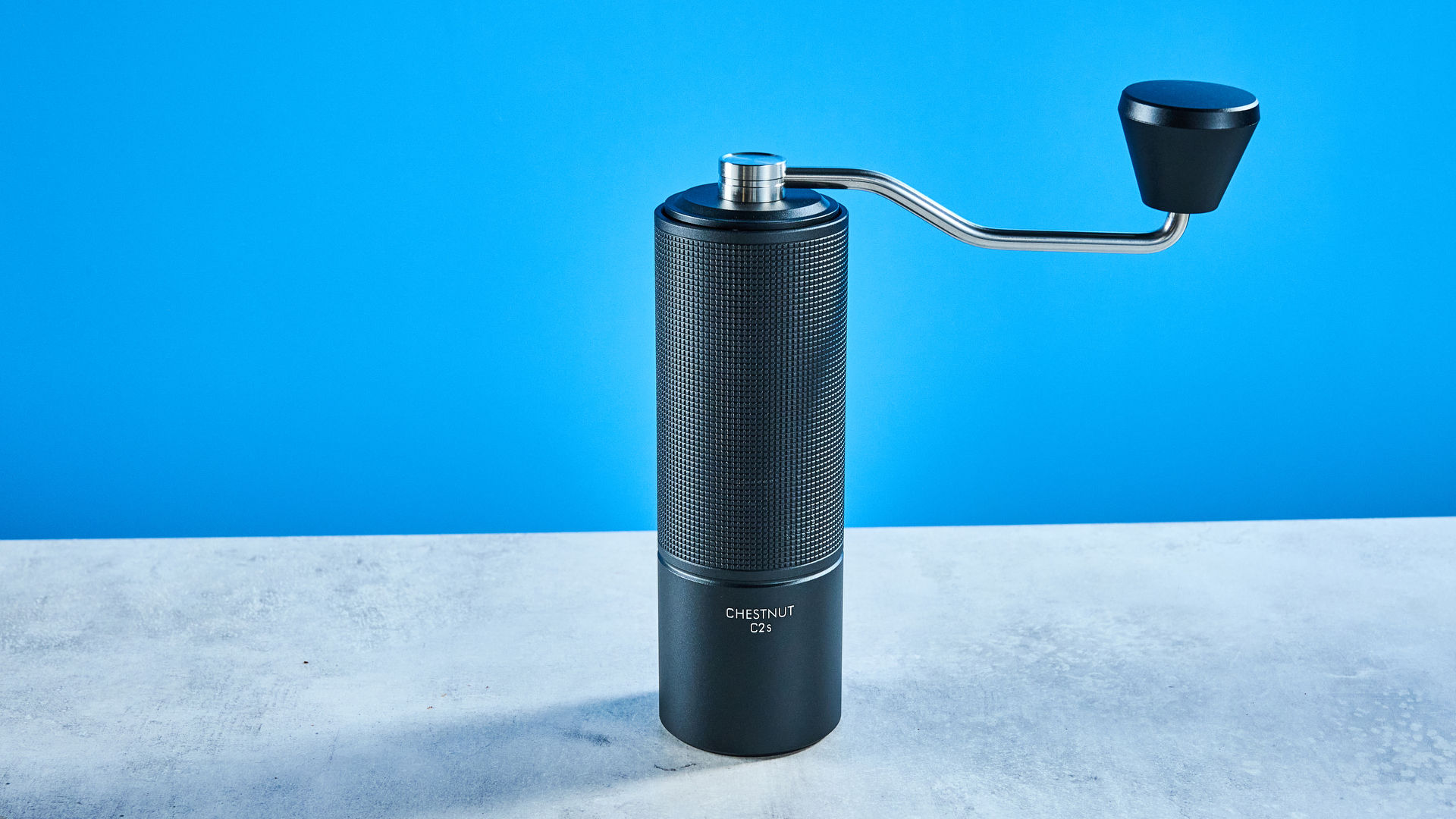 the timemore chestnut c2s coffee grinder in black showing its hand crank and catch chamber photographed against the blue tom's guide background