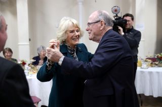 Queen Camilla dancing with Arthur Edwards at a 2017 tea party as people watch on at tables