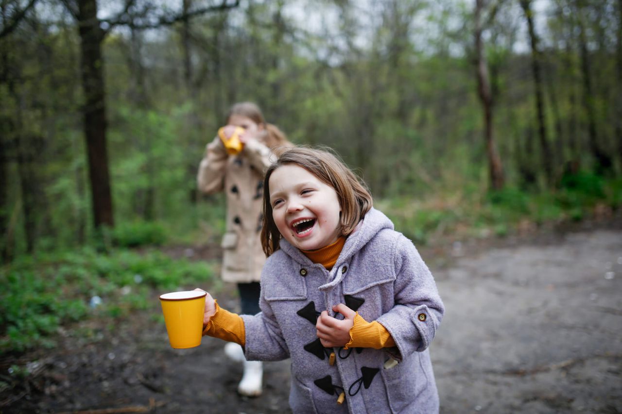 Children sisters in autumn coats drink hot tea in forest. little girls friends drinking water in the woods. Sisters having picnic in forest on Winter&#039;s day.