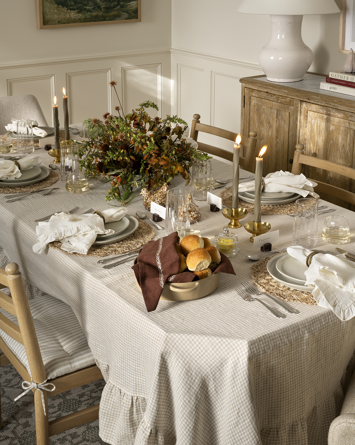McGee &amp;amp; Co. fall table decor, including a silver fluted pie server, ceramic pie dish, woven plate charger, ruffle-border napkins, metallic candleholders, and a gingham tablecloth, in a white-walled dining room