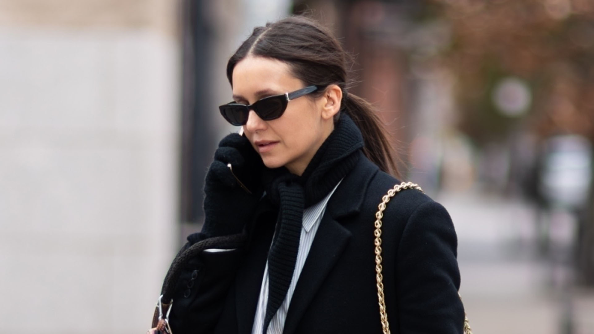 Nina Debrov wearing a black coat, white striped button down, black scarf, and snakeskin shoes