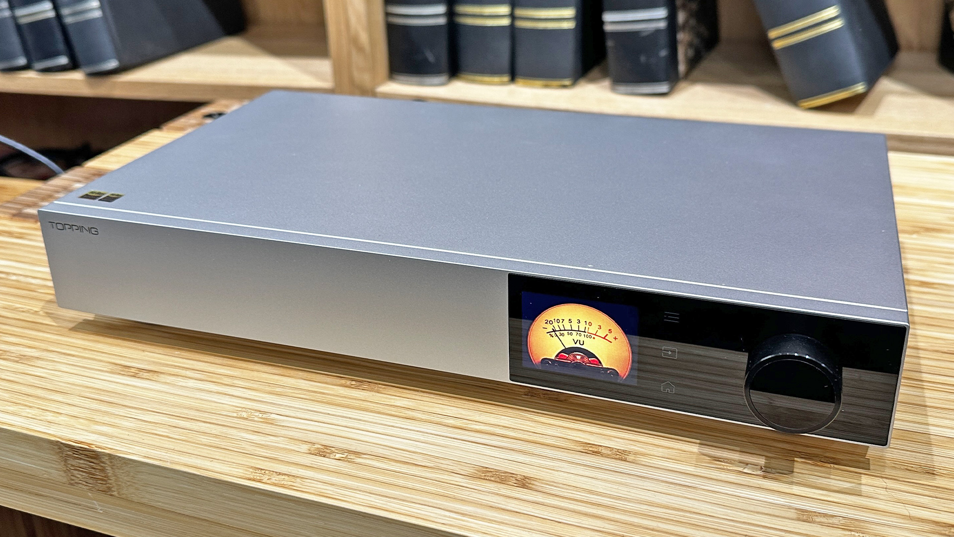 Topping Audio D900 DAC on wooden hi-fi rack in front of bookcase, on display is VU meter