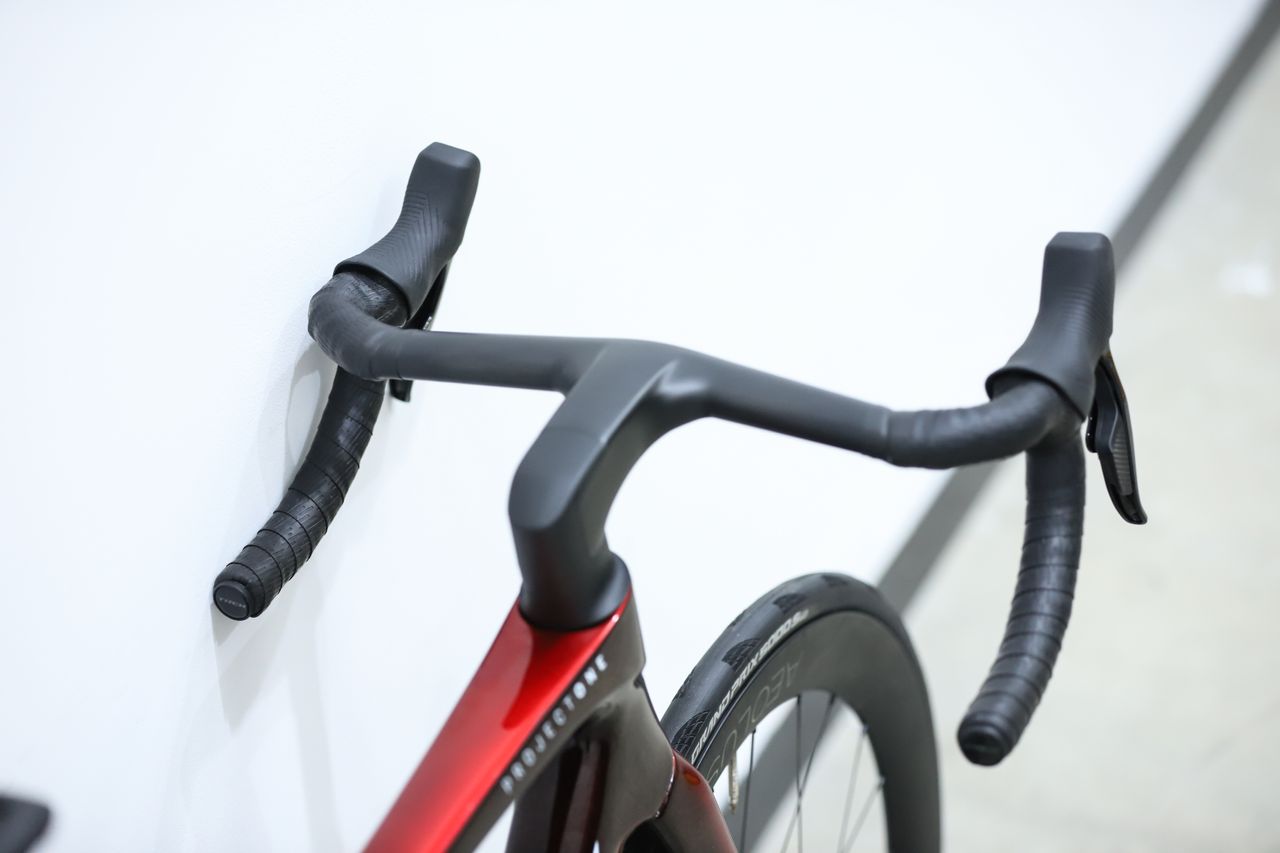 A red Trek Madone SLR 7 (gen 8) stands against a white wall