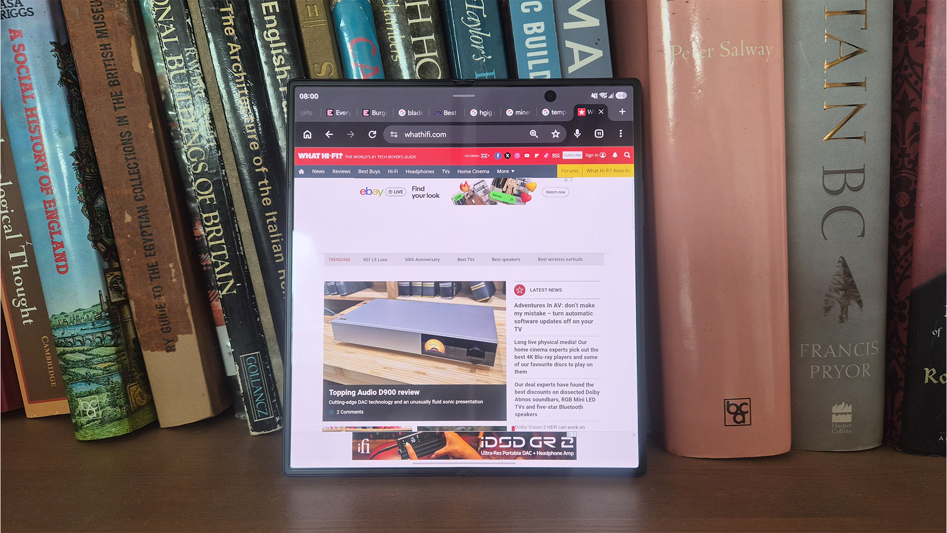Samsung Z Fold 8 Ultra smartphone unfolded on bookcase, on screen is What Hi-Fi? website page