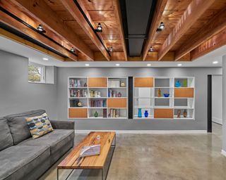 Basement with grey sofa and coffee table and open bookcase with gray walls and neutral floor