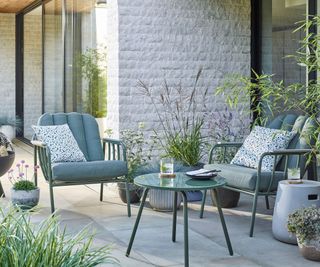 A beautiful mint green outdoor seating set with low chairs and bistro table on a patio with plant pots filled with flowers