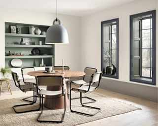 Dining room with round wooden table, modern chairs, white walls and grey window frames as well as sage green built-in shelves