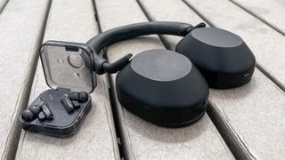 The Sony WH-1000XM5 laying on the ground next the Nothing Ear wireless earbuds.