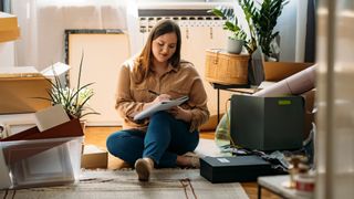 Woman making a list on paper in living room among boxes