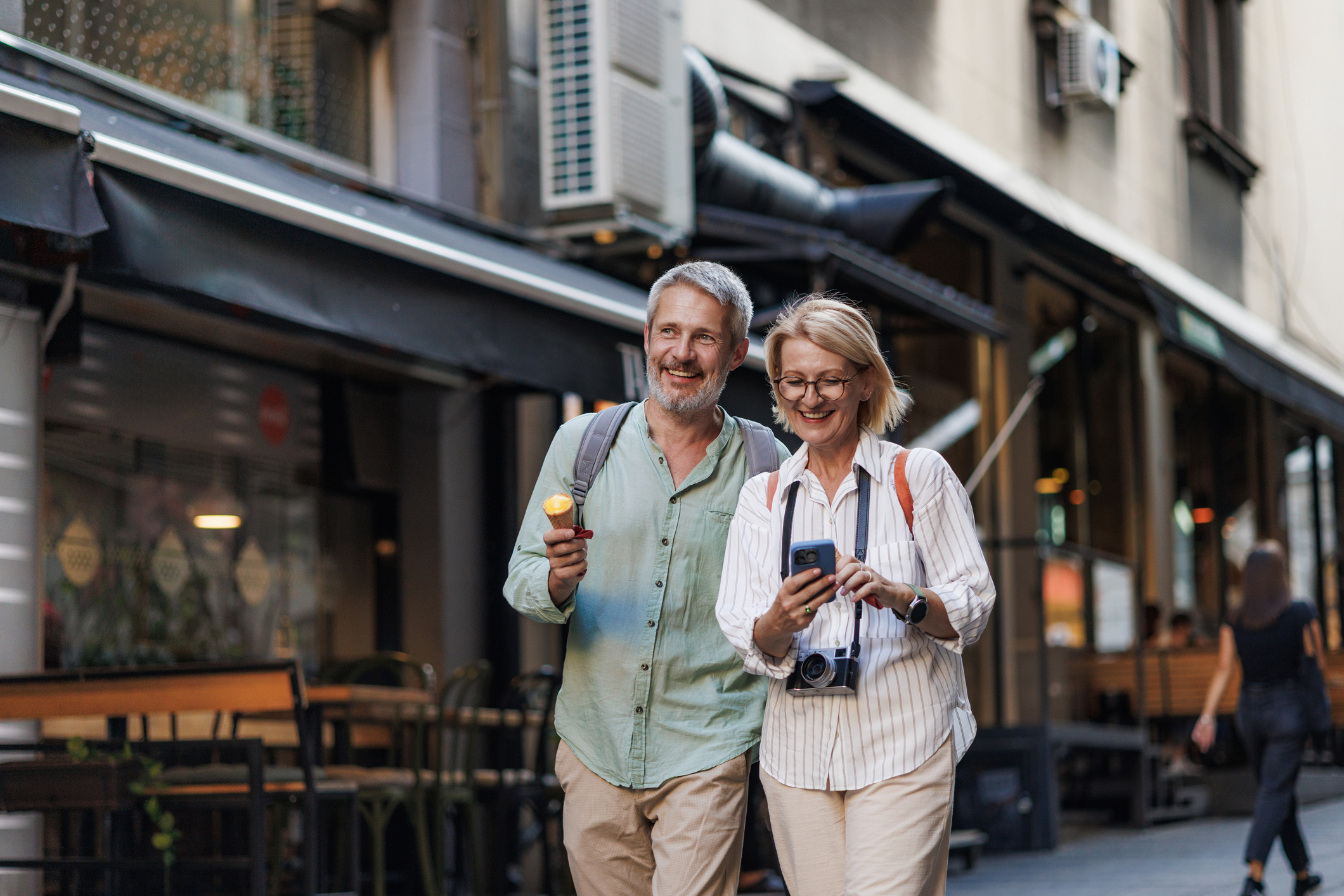 Smiling mature couple walking down a city street while eating ice cream cones, embodying togetherness and relaxation.