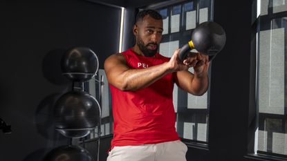 Man weaing red vest exercising with a kettlebell in a gym