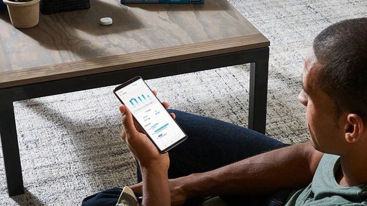 SmartThings Energy app being used on a smartphone while a man sits in a lounge