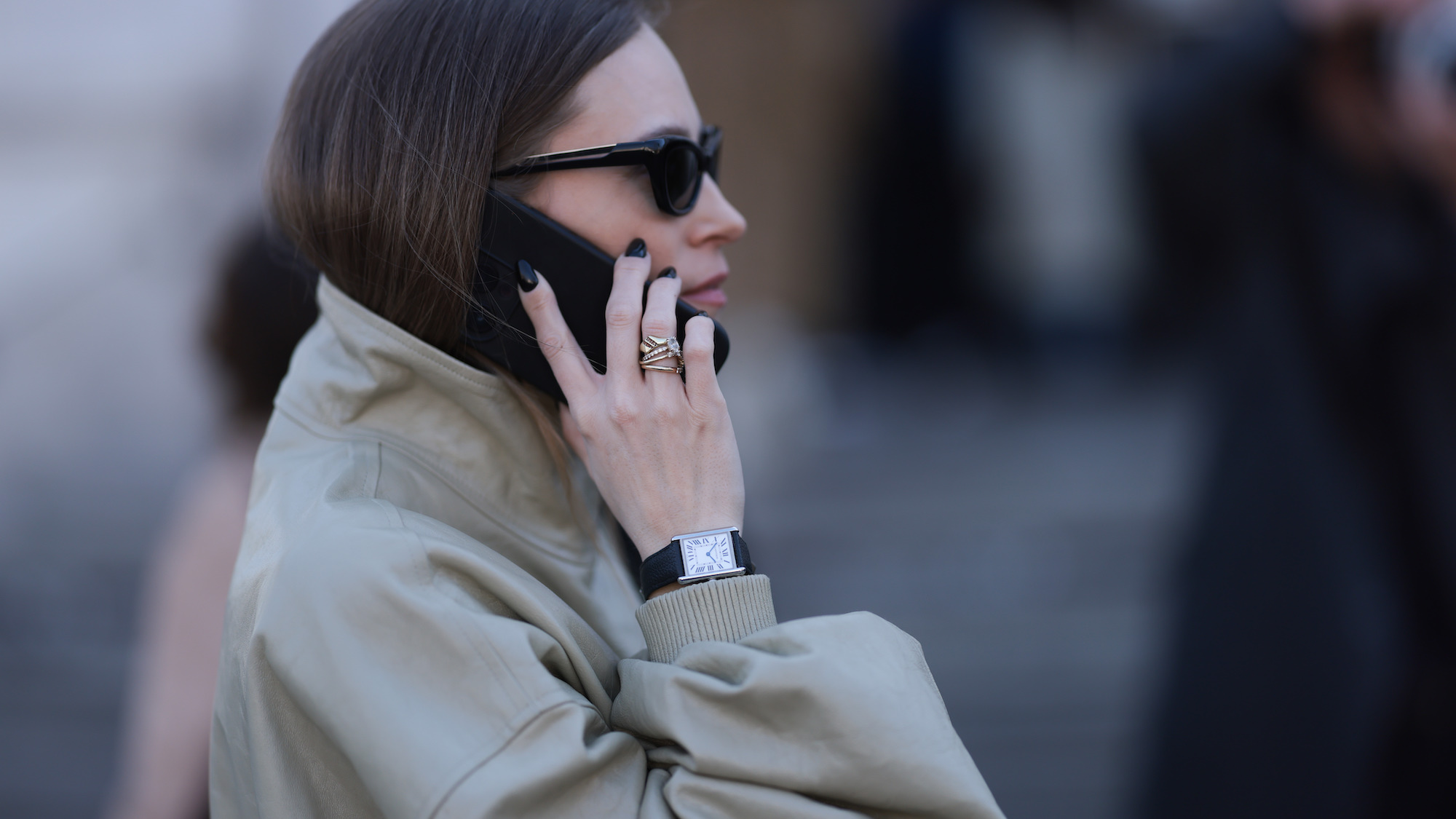 Brunette woman wearing a khaki jacket, sunglasses, and black nails