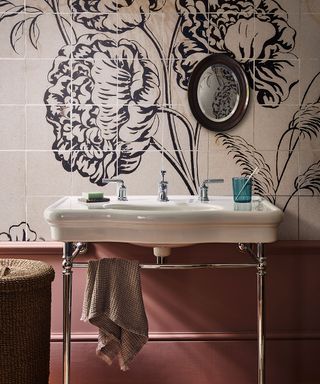 A bathroom with wall tiles laid to create a floral pattern behind a traditional white sink
