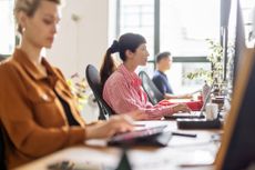 Woman working on laptop sitting at coworking desk with colleagues at startup office