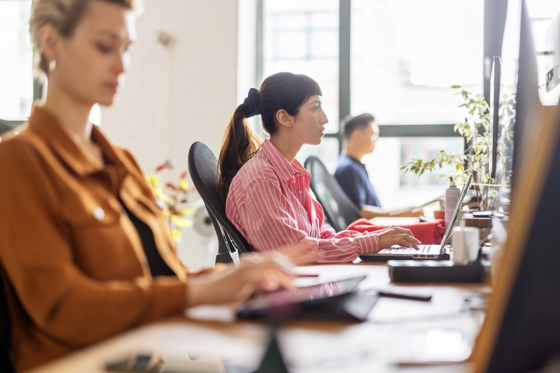 Woman working on laptop sitting at coworking desk with colleagues at startup office