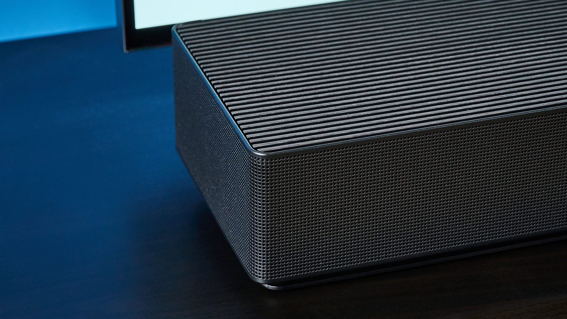 the samsung qs90h soundbar in a living room set with a tv and photographed with the blue tom's guide background