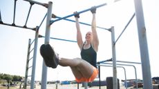 woman in 40s hangs from calesthenics bar mid pull-up exercise