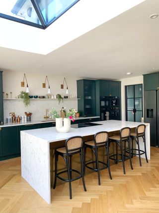 Marble kitchen island/breakfast bar with cane backed bar stools, forest green cabinetry and copper accents