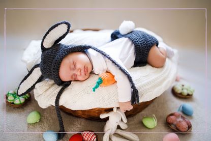 A newborn baby in a basket wearing bunny ears and a tail surrounded by Easter eggs