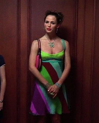 Jenna from 13 Going on 30 wearing a colorful striped dress, a butterfly necklace, and a pink shoulder bag.