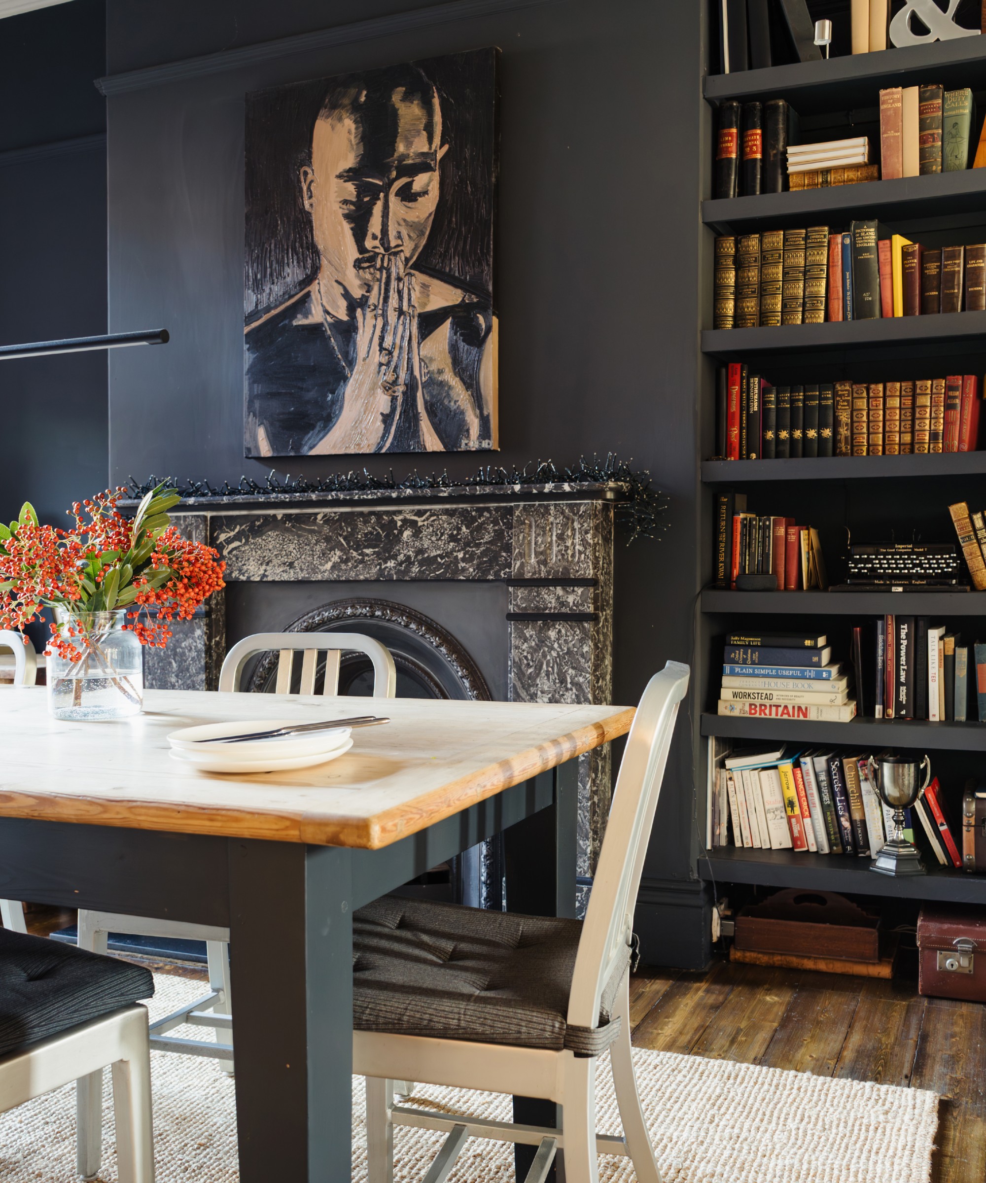 A black-painted dining area with a marble fireplace and a large portrait artwork hanging above it