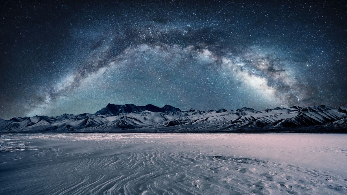 a starry night sky over snow-capped mountains