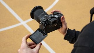 Nikon Z6 III camera in the hand from over the photographer's shoulder with flip-touchscreen out