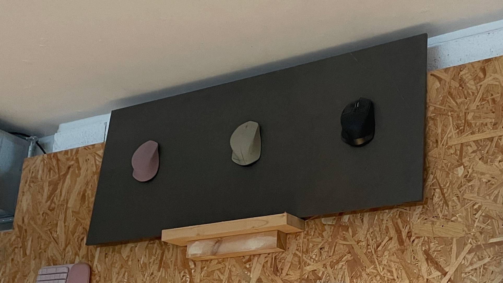 A range of Logitech MX Master 2 mouse prototypes, including a wooden one, on a wall.