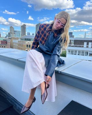 Tori wears pink skirt, long-sleeve leather top, and burgundy slingbacks.