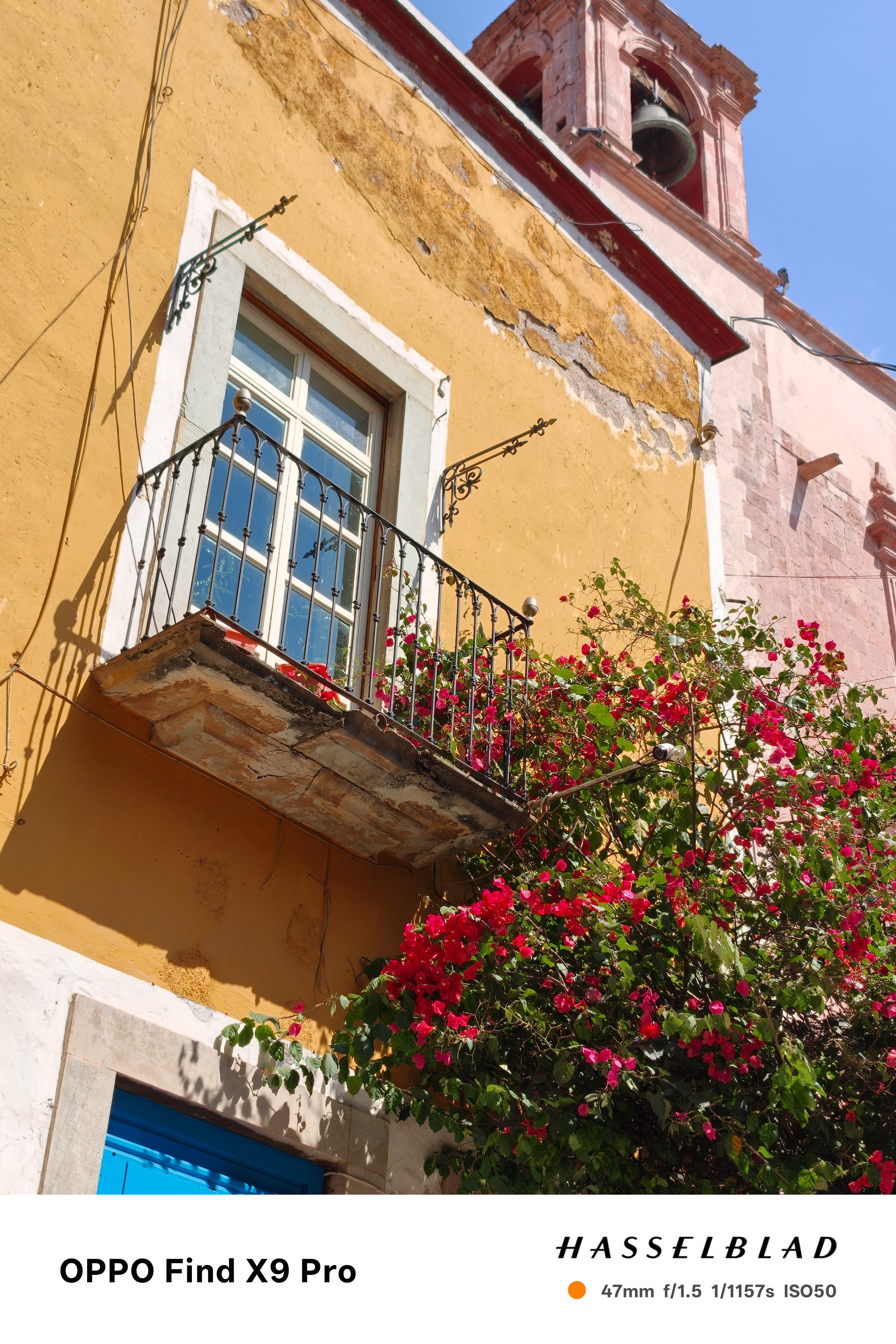 A colourful yellow house with a balcony and red flowers