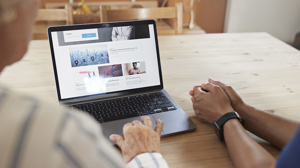 Two people look over an open laptop that&#039;s showing a website builder. 