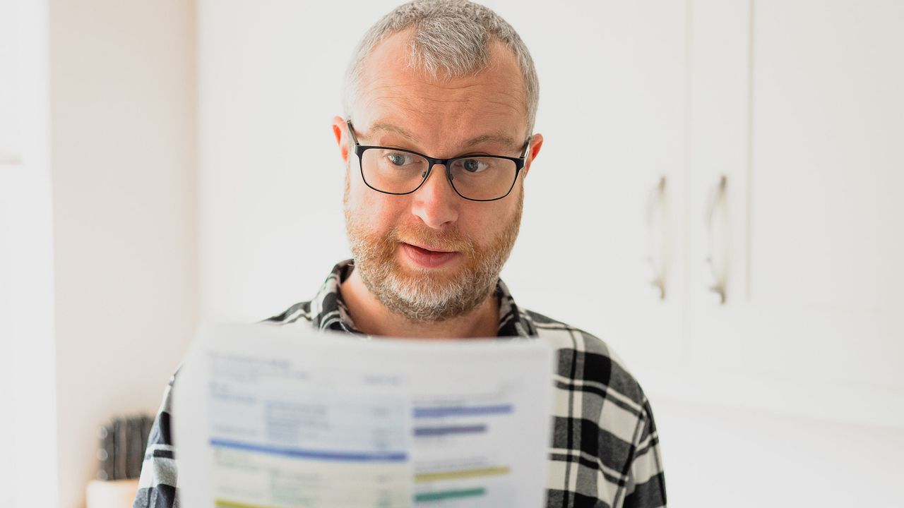 A man wearing glasses closely looks at a paper with numbers.