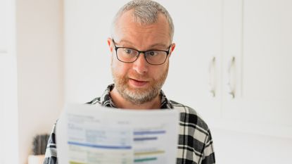 A man wearing glasses closely looks at a paper with numbers.