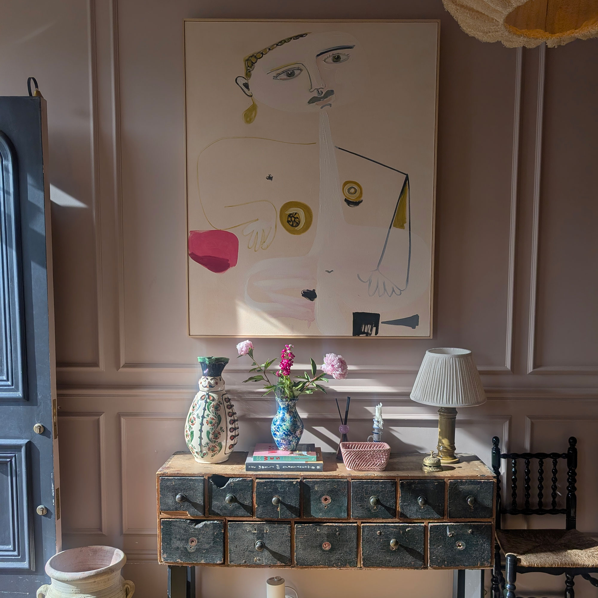 Hallway with pale pink panelled walls, graphic artwork and vintage apothecary style console table