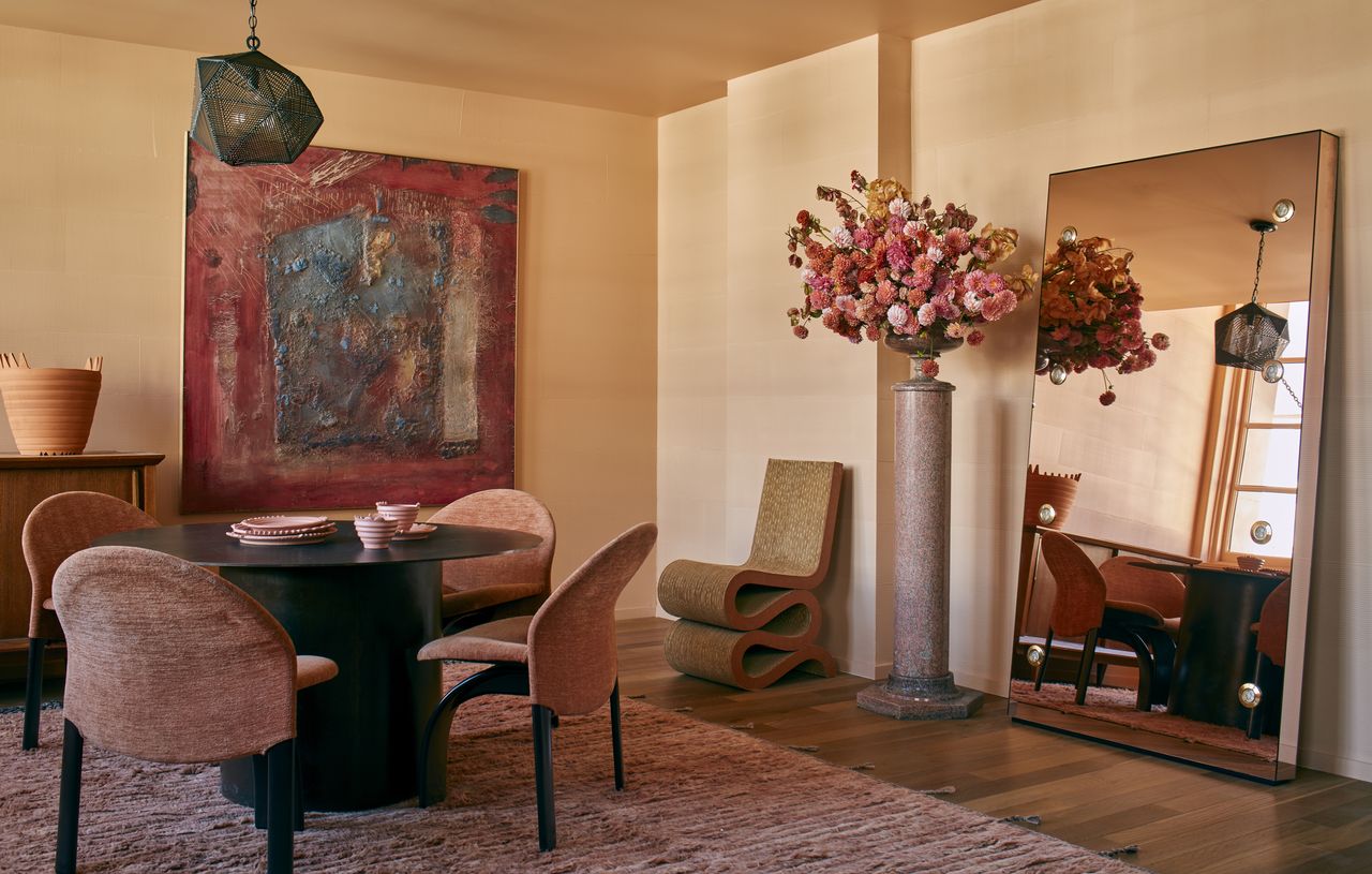 A pink dining room with a circular table, a large area rug, and a large mirror leaning against the wall