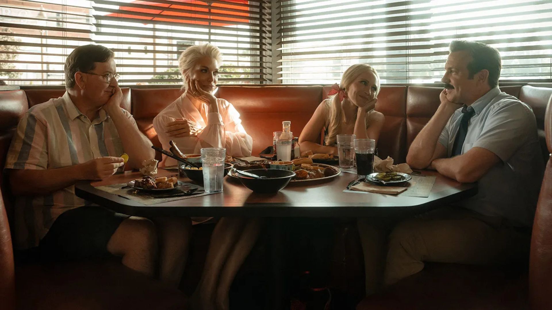 Hannah Waddingham (Rebecca Welton), Juno Temple (Keeley Jones) and Jeremy Swift (Leslie Higgins) looking at Jason Sudeikis (Ted Lasso) around a diner table