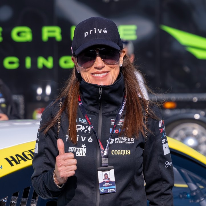 Racecar driver and Privé founder Shay Hoelscher gives a thumb up while wearing her racing outfit.
