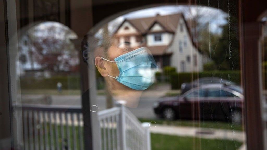 A woman wearing a surgical mask looks out of a window.