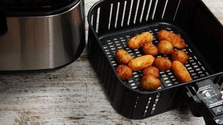 an air fryer and an air fryer basket with fried food in it, on a kitchen worktop