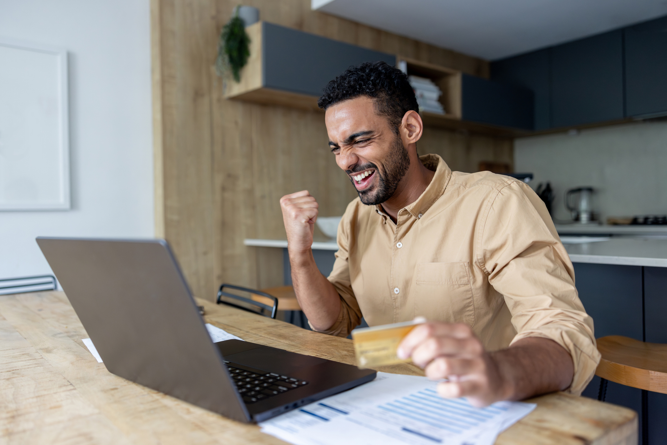 Premium Bonds holder celebrates winning as he looks at laptop and holds debit card.