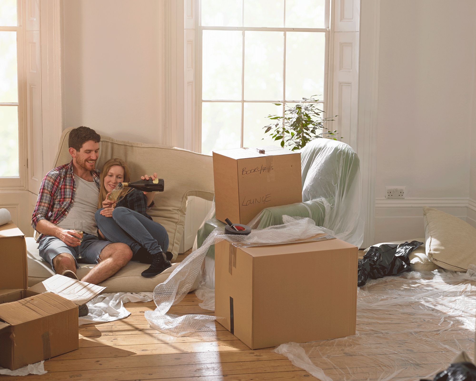 young couple surrounded by moving boxes drinking bubbly on moving day