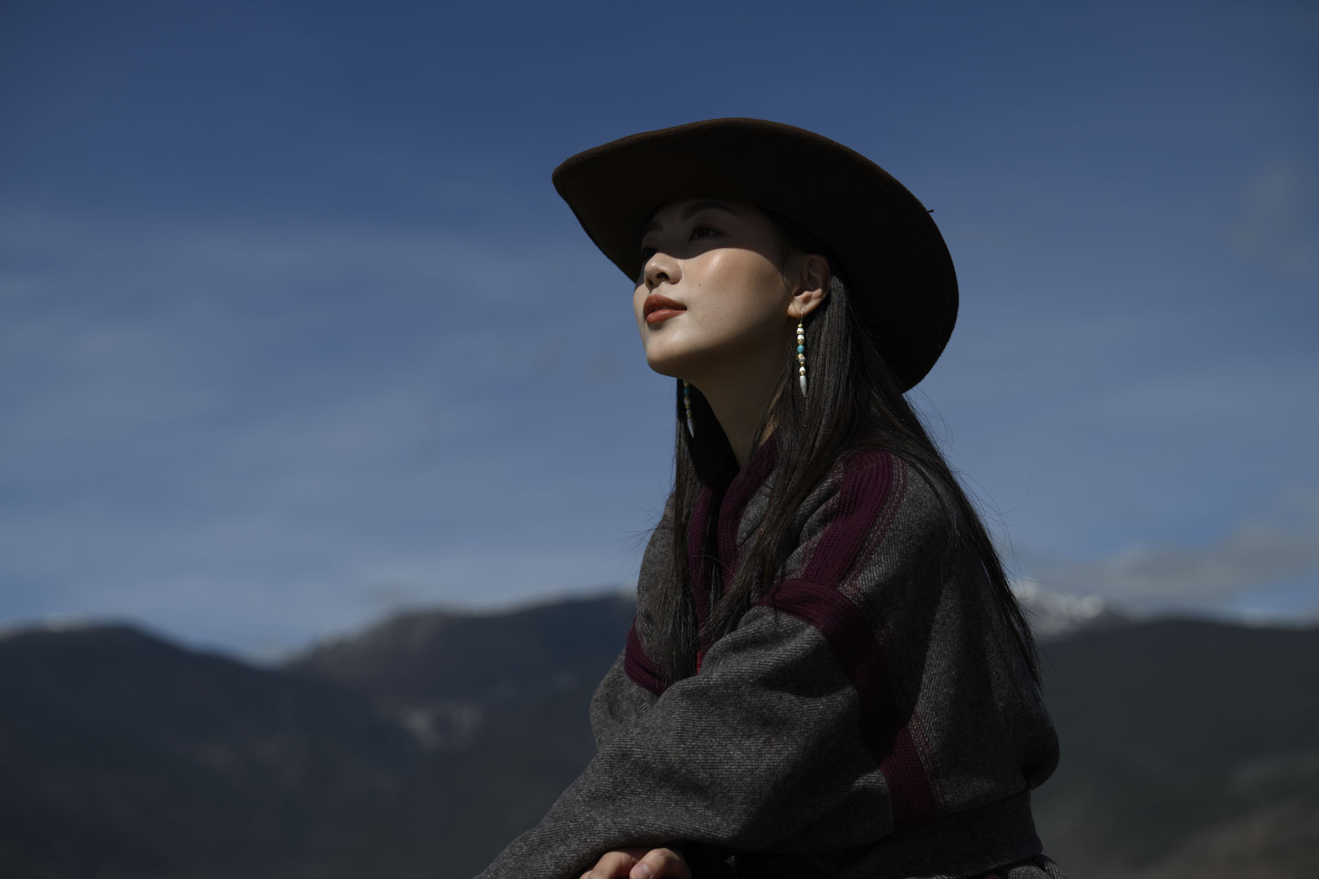 Nikon Z 70-200mm f/2.8 VR S II image gallery: a female model in a cowboy hat in bright sunlight, there's snow-covered mountaintops behind her