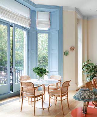 dining area with blue shutters, windows and doors, white blinds, white Tulip table and rattan chairs