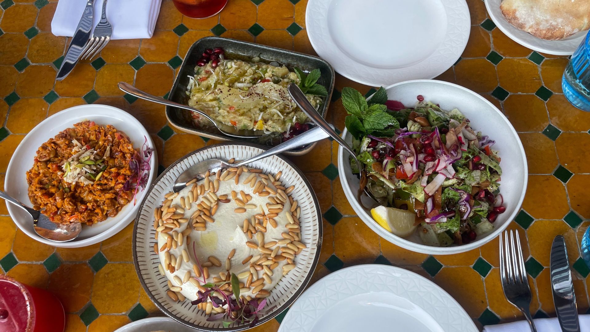 an image of the author's table full of food, with a range of cold mezze including hummus, fatoush, Muhamarah, and Moutabal