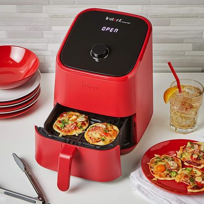 Red Instant Vortex Mini Air Fryer with open drawer containing 2 mini pizzas next to a red plate with mini pizzas