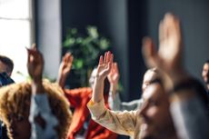 An anonymous group of people raising hands in a meeting, asking questions.