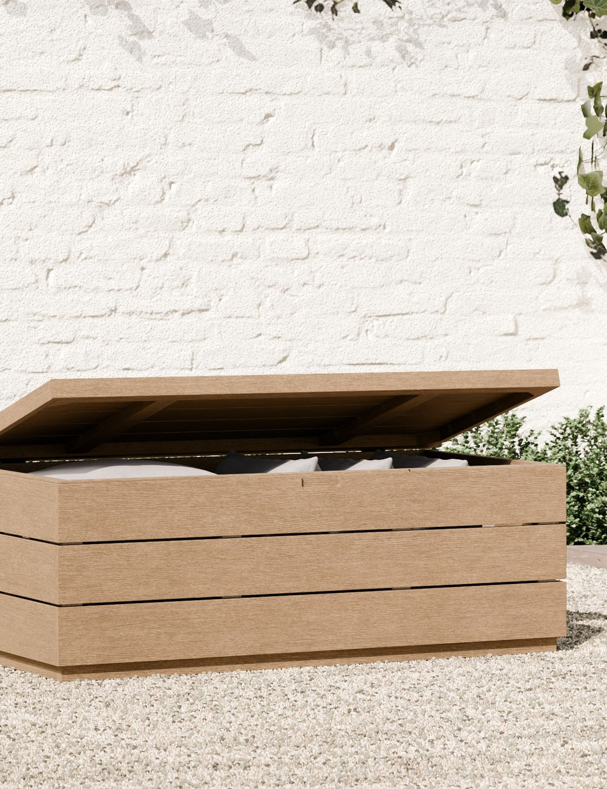 Wooden West Elm outdoor storage trunk seen with its lid up, exposing the spare patio cushions it's stashing inside